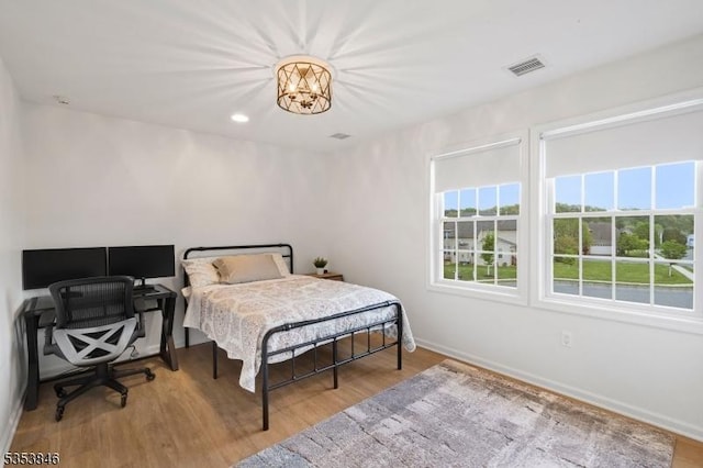 bedroom with baseboards, an inviting chandelier, visible vents, and wood finished floors