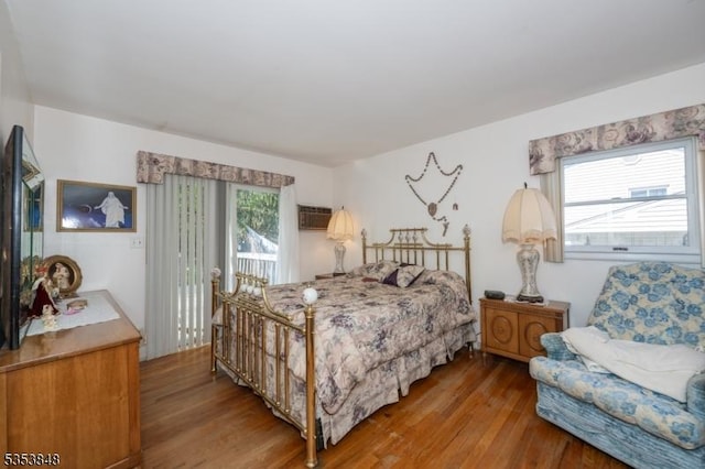 bedroom with access to outside, a wall mounted AC, and wood finished floors