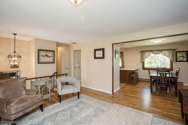 living area featuring baseboards, a baseboard heating unit, wood finished floors, and a notable chandelier
