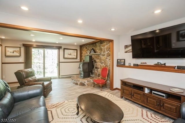 living room featuring recessed lighting, baseboards, a wood stove, and light wood finished floors