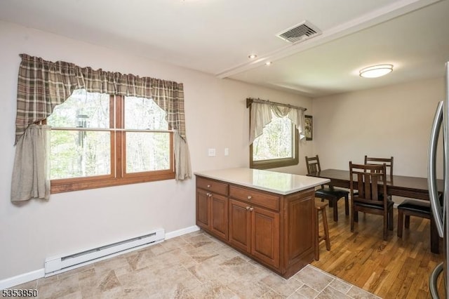 kitchen with visible vents, brown cabinetry, a peninsula, light countertops, and a baseboard heating unit