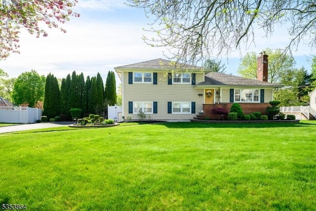 tri-level home featuring brick siding, fence, a chimney, and a front lawn