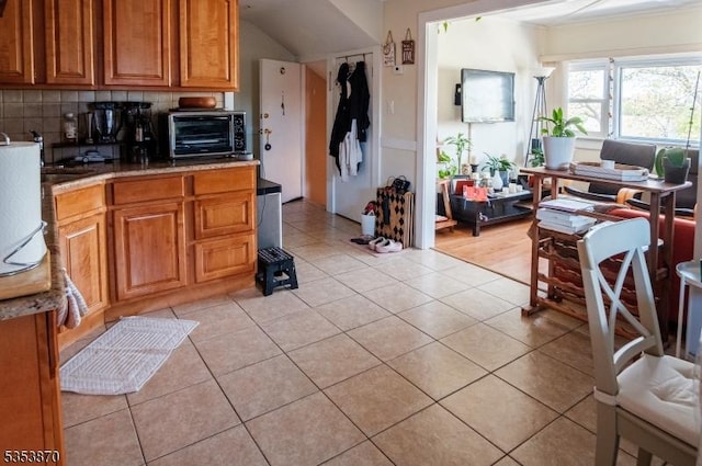 kitchen with a toaster, light tile patterned floors, tasteful backsplash, and brown cabinets