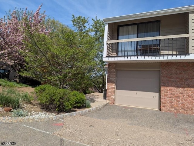 view of front facade featuring a balcony, an attached garage, driveway, and brick siding