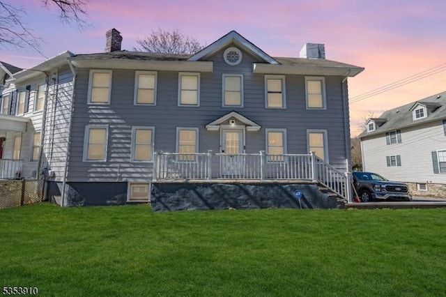 view of front facade featuring a lawn, a chimney, and a porch
