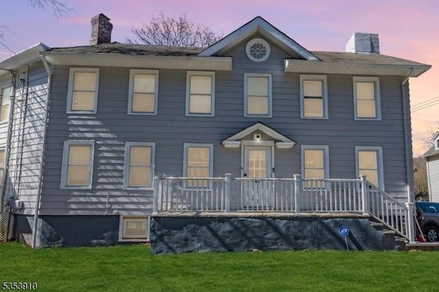 colonial-style house with covered porch, a chimney, and a yard