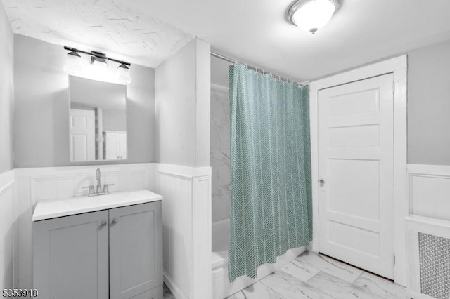 bathroom with wainscoting, a decorative wall, vanity, shower / bath combo with shower curtain, and marble finish floor
