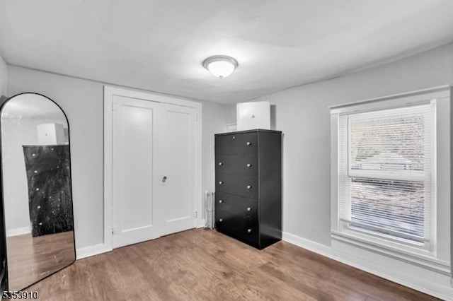unfurnished bedroom featuring baseboards, wood finished floors, and a closet