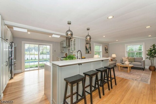 kitchen featuring wall chimney range hood, glass insert cabinets, recessed lighting, and light wood-style flooring