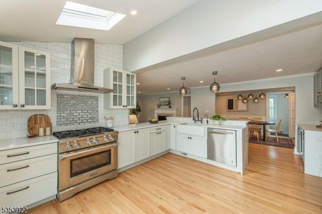 kitchen featuring light wood finished floors, wall chimney exhaust hood, stainless steel appliances, a peninsula, and tasteful backsplash