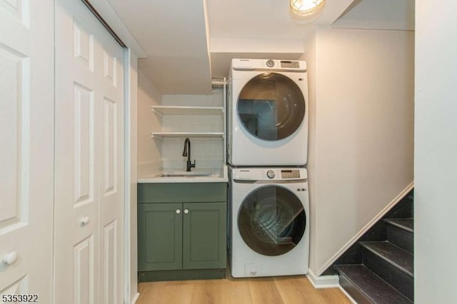 washroom with light wood-style floors, stacked washer and clothes dryer, a sink, and cabinet space