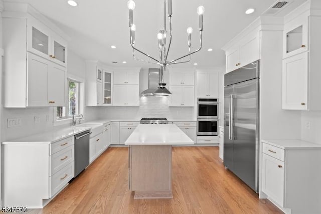 kitchen featuring wall chimney range hood, a kitchen island, visible vents, white cabinets, and stainless steel appliances