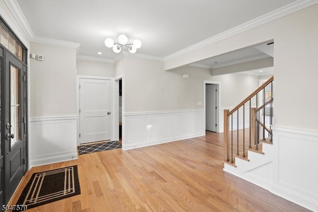 entryway with an inviting chandelier, wainscoting, light wood-type flooring, ornamental molding, and stairway