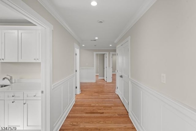 corridor with crown molding, a decorative wall, recessed lighting, a wainscoted wall, and a sink