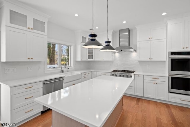 kitchen with wall chimney range hood, appliances with stainless steel finishes, light wood-style flooring, and light countertops