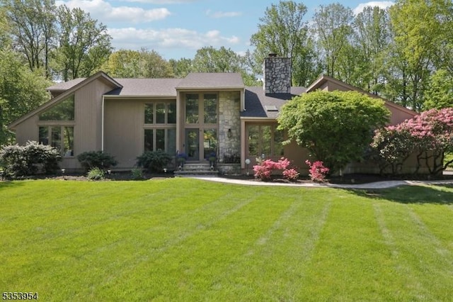 rear view of property with a chimney, a yard, and stone siding