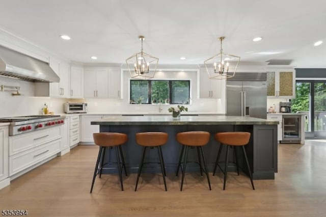 kitchen with appliances with stainless steel finishes, a chandelier, a center island, wall chimney range hood, and a sink