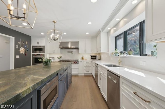 kitchen with stainless steel appliances, a chandelier, a sink, range hood, and white cabinets