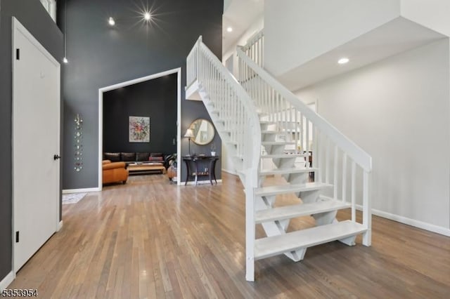 staircase featuring a towering ceiling, wood finished floors, baseboards, and recessed lighting
