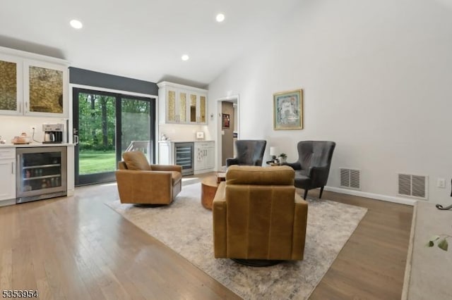 living area featuring bar area, beverage cooler, vaulted ceiling, wood finished floors, and recessed lighting