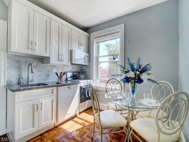 kitchen with a sink, white cabinetry, white appliances, and tasteful backsplash