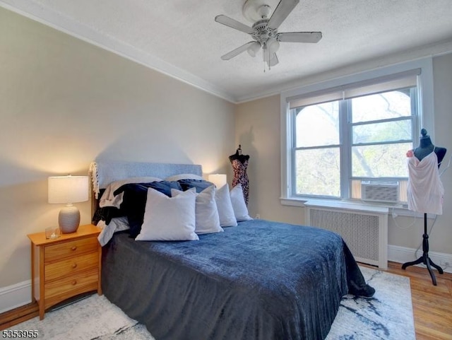bedroom with ceiling fan, baseboards, radiator heating unit, ornamental molding, and light wood-style flooring