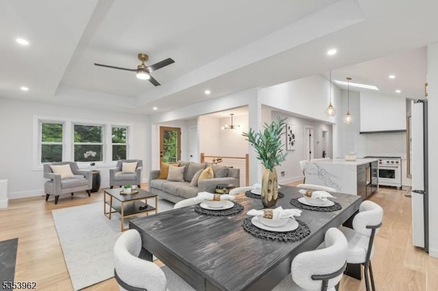 dining area with a tray ceiling, light wood finished floors, ceiling fan, recessed lighting, and baseboards
