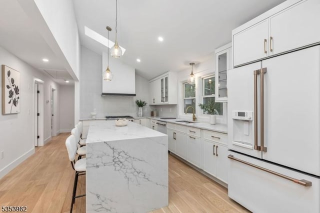 kitchen featuring high end white refrigerator, a center island, a sink, white cabinetry, and glass insert cabinets