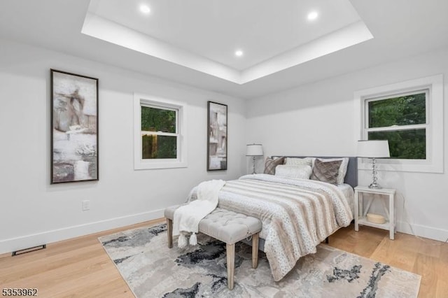 bedroom with a tray ceiling, baseboards, light wood-type flooring, and recessed lighting