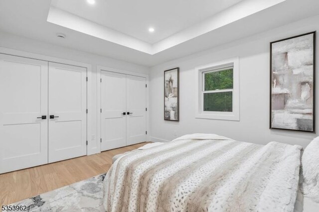 bedroom featuring two closets, light wood-style flooring, recessed lighting, and a raised ceiling
