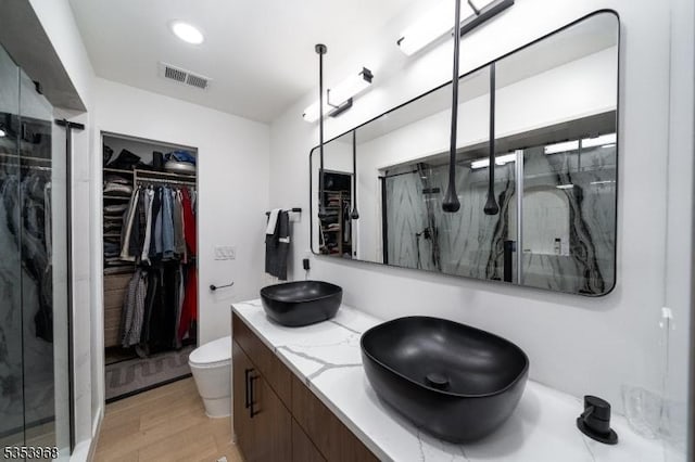 bathroom with a sink, a shower stall, wood finished floors, a spacious closet, and visible vents