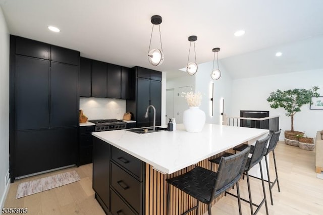 kitchen with decorative light fixtures, light wood-type flooring, a sink, dark cabinetry, and a breakfast bar