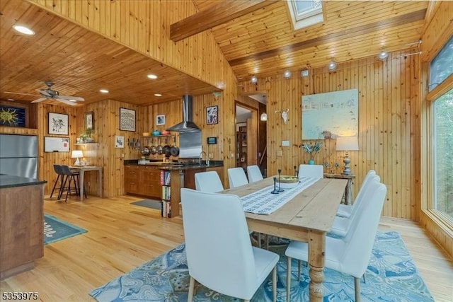 dining area featuring wood walls, light wood-style floors, wood ceiling, ceiling fan, and a skylight
