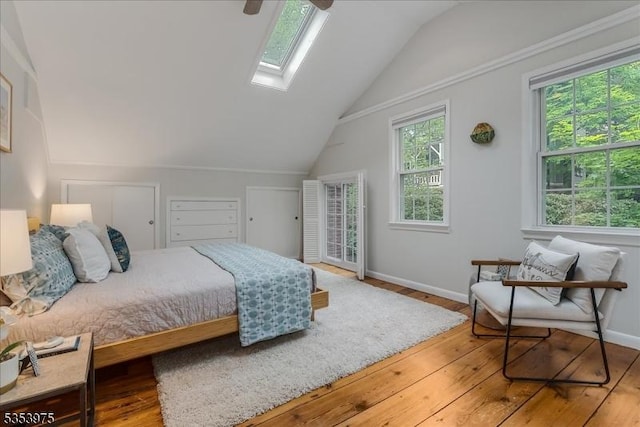 bedroom with a skylight, vaulted ceiling, hardwood / wood-style floors, baseboards, and ceiling fan