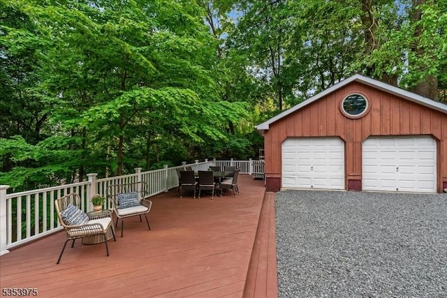 deck featuring a detached garage, outdoor dining area, and view of wooded area