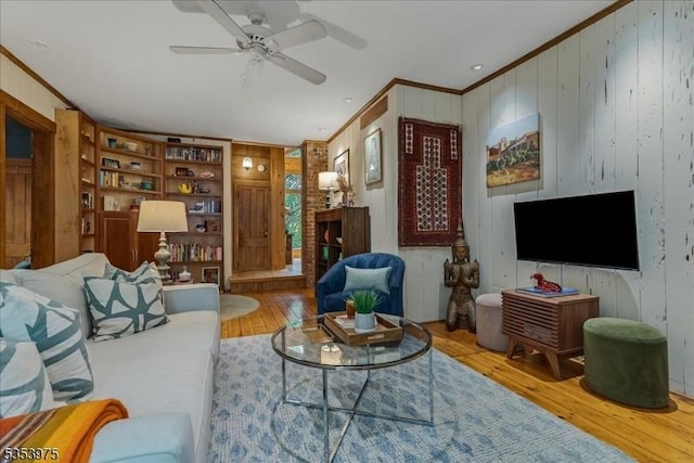 living area featuring ornamental molding, hardwood / wood-style flooring, wooden walls, and ceiling fan
