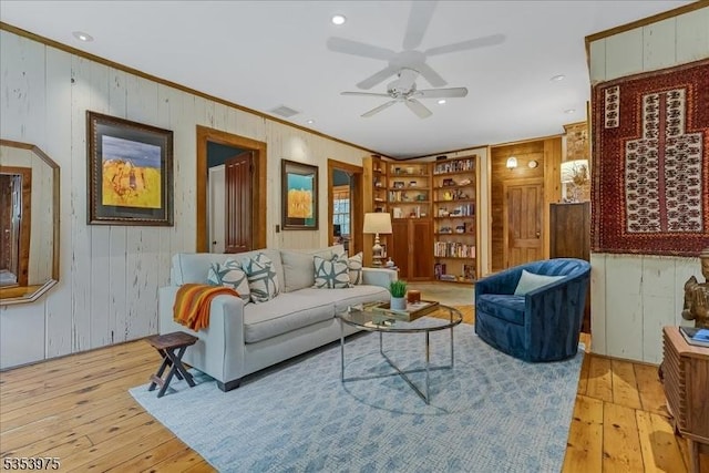 living area with wooden walls, ornamental molding, built in shelves, hardwood / wood-style floors, and ceiling fan