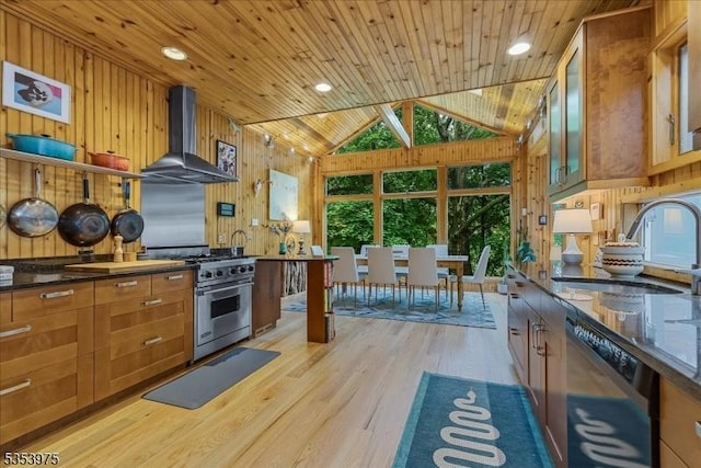 kitchen featuring black dishwasher, stainless steel range, wall chimney exhaust hood, a sink, and wooden walls
