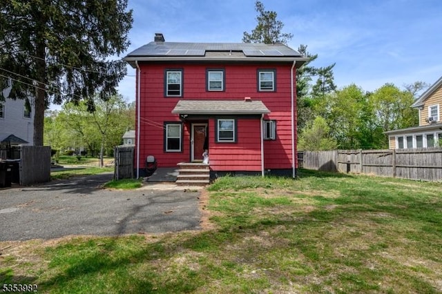 view of front facade with fence, a chimney, solar panels, and a front lawn