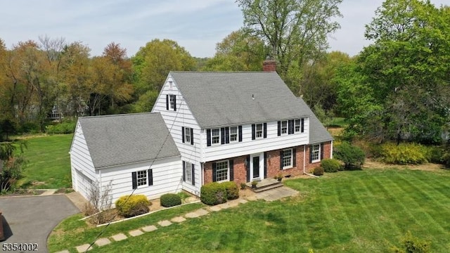 view of front of home featuring brick siding, a chimney, a shingled roof, and a front lawn