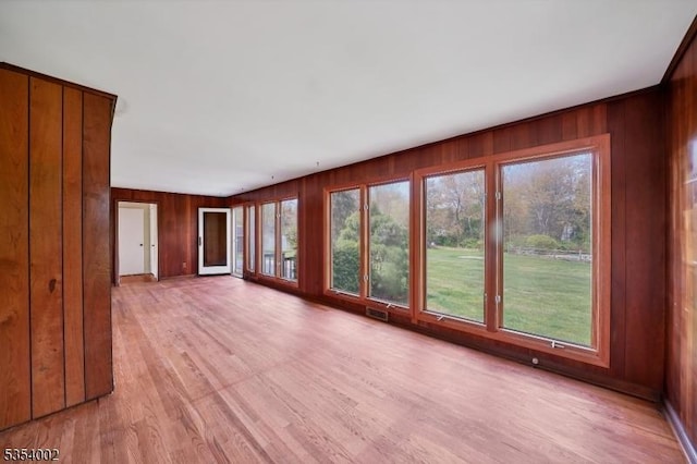 unfurnished living room with visible vents, light wood-style flooring, and wooden walls
