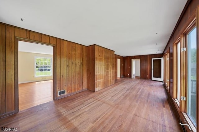 spare room featuring baseboards, wood walls, visible vents, and wood finished floors