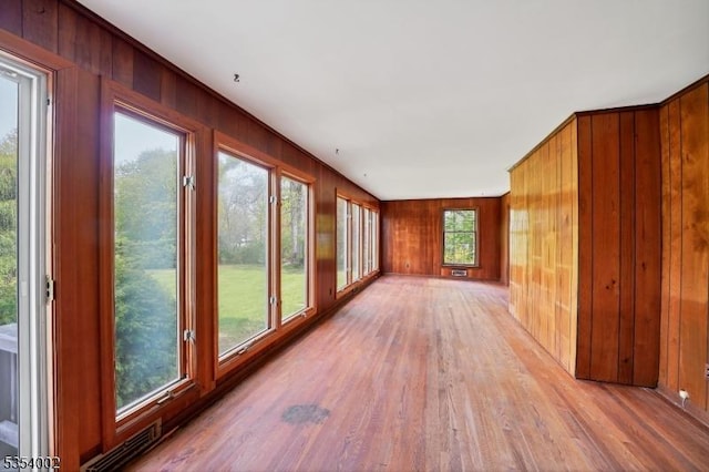 unfurnished sunroom featuring wood walls, wood finished floors, and visible vents