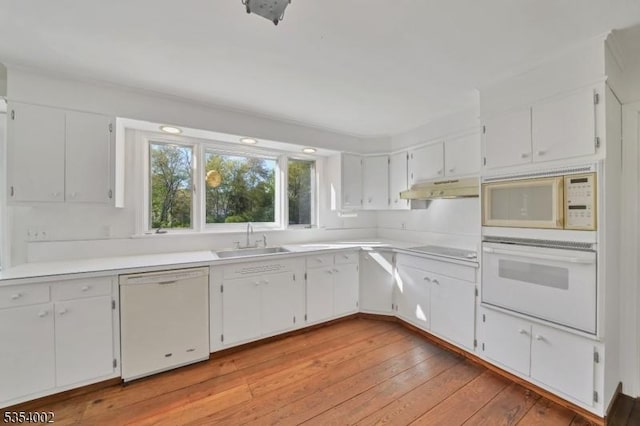 kitchen with a sink, white appliances, light wood-style flooring, white cabinetry, and under cabinet range hood