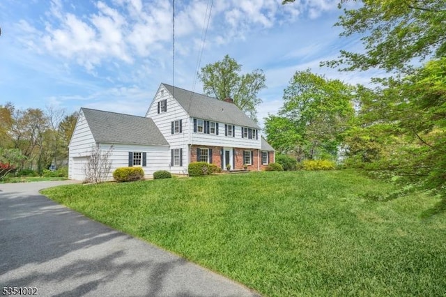 view of front of home with a shingled roof, an attached garage, a front lawn, and aphalt driveway
