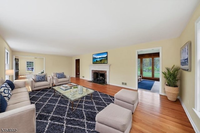 living room featuring plenty of natural light, a brick fireplace, light wood-style flooring, and visible vents