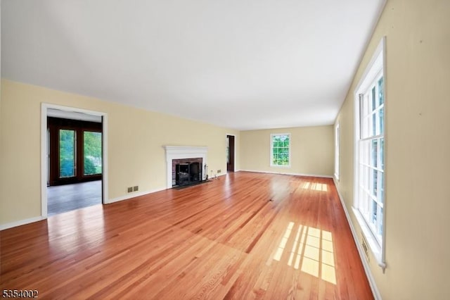 unfurnished living room featuring light wood-type flooring, baseboards, a brick fireplace, and visible vents