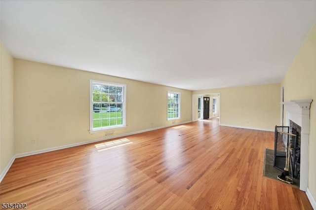 unfurnished living room featuring baseboards, a fireplace with flush hearth, and light wood-style floors
