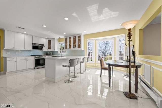 kitchen featuring a kitchen breakfast bar, stainless steel appliances, recessed lighting, a baseboard radiator, and glass insert cabinets