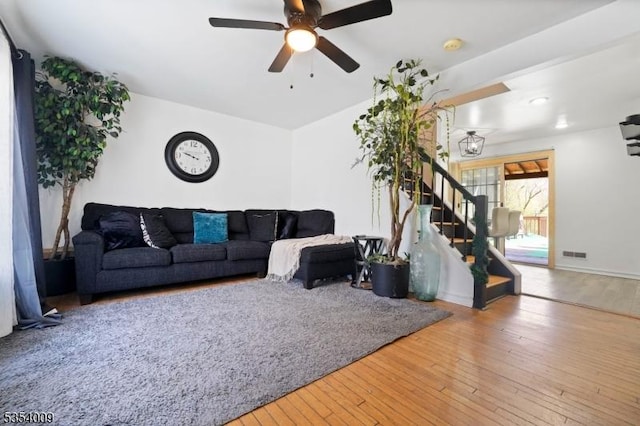 living area with wood-type flooring, ceiling fan, visible vents, and stairway
